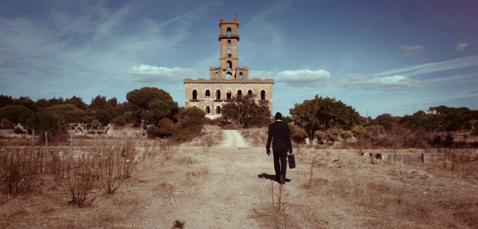 Cinematic film still from 'Lisboa', showing Rupert Jaeger wearing a dark suit and balaclava, walking towards the legendary Palácio do Rei do Lixo (Torre de Coina)